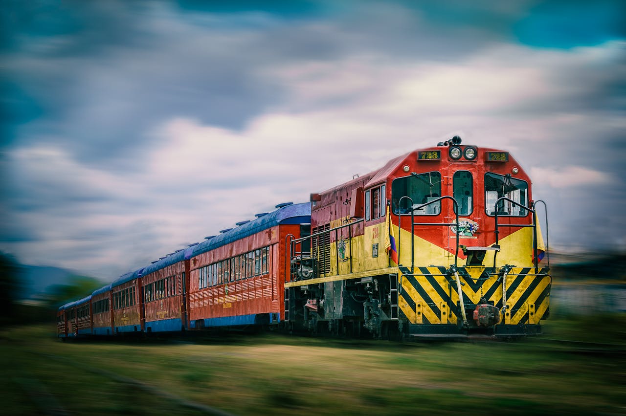 A vibrant red train speeding along the tracks with blurred motion under a bright sky.