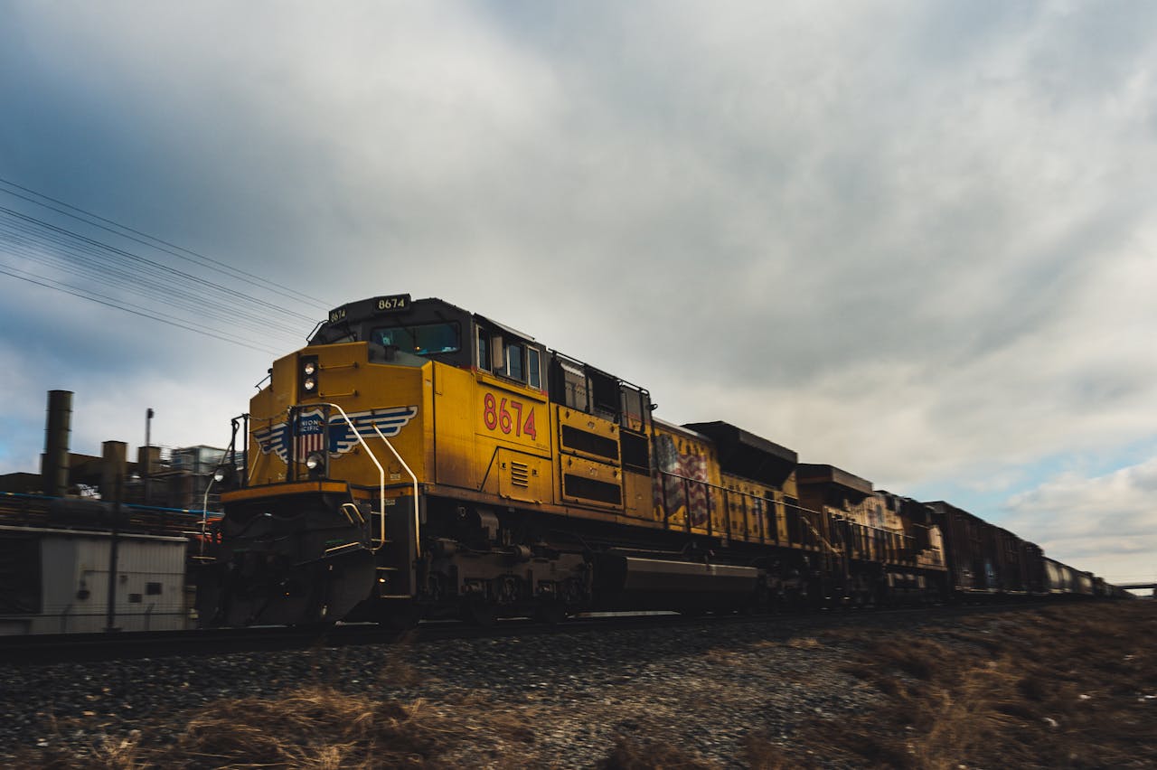 Yellow freight train moving on outdoor railway track under cloudy sky.